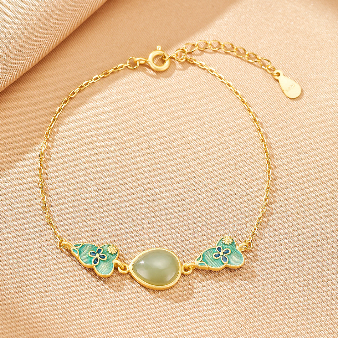 Gold plated silver bracelet featuring a smooth, oval, light green jade stone set between two light blue enamel cloud charms with floral accents.