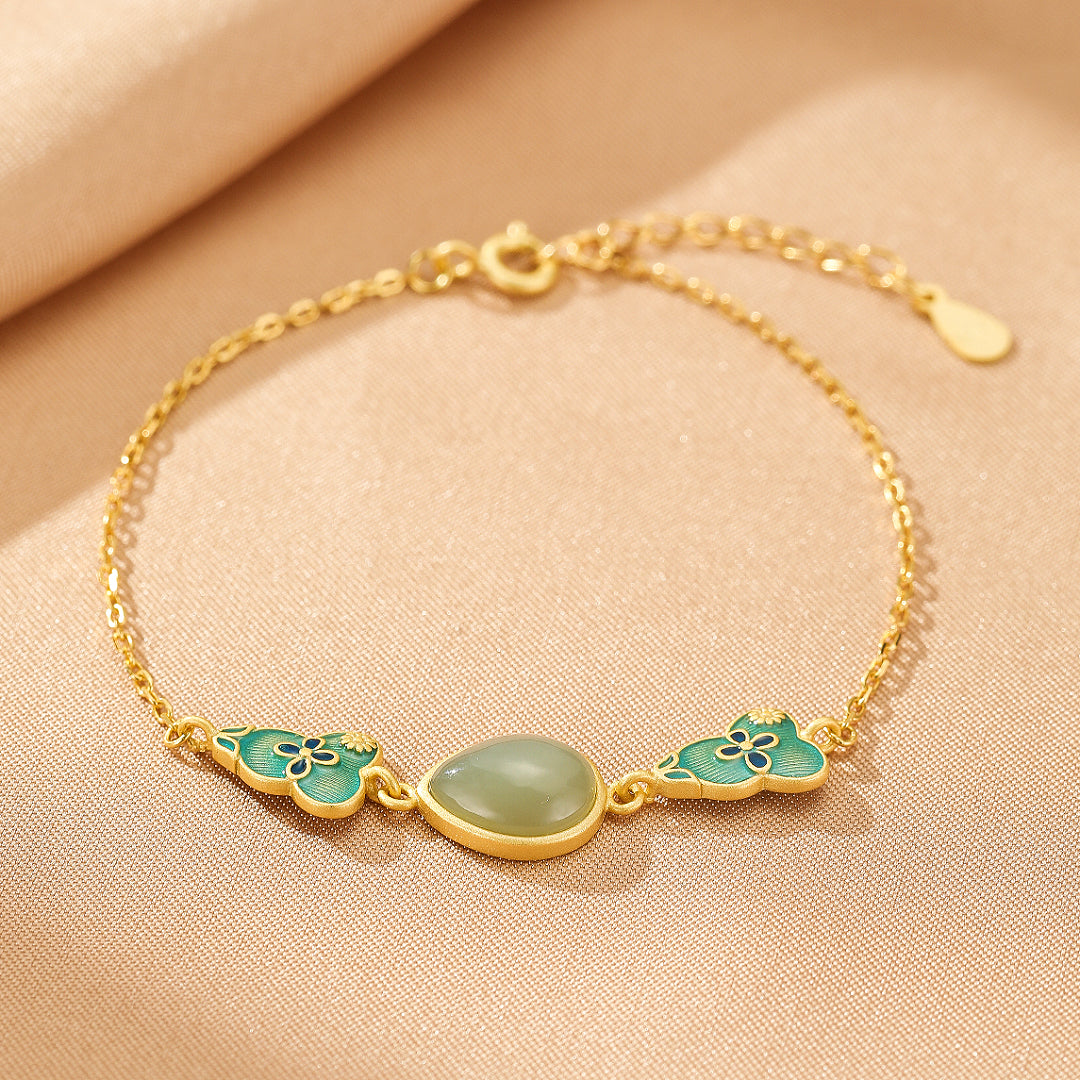 Gold plated silver bracelet with a teardrop-shaped light green jade stone and blue cloud-shaped charms on a delicate chain.