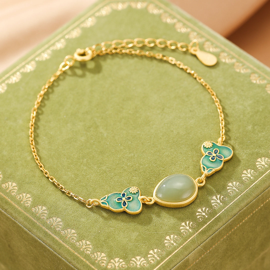 Gold-plated silver bracelet featuring a smooth, oval Hetian jade stone accented by two gourd-shaped charms with blue floral enamel details.