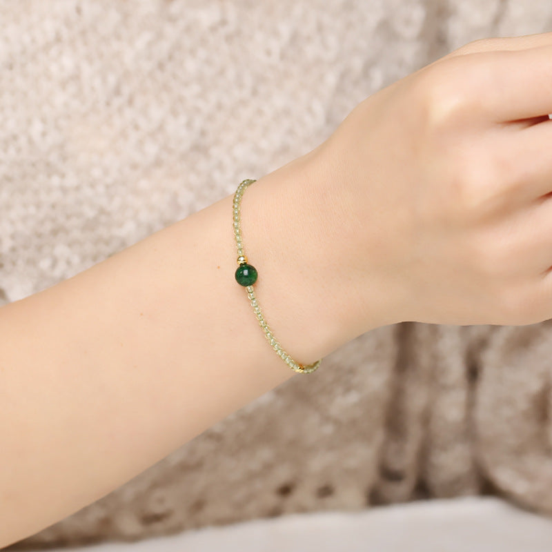 Close-up of a delicate bracelet on a woman's wrist, featuring small light green beads and a single, larger deep green jade bead with a small gold accent.