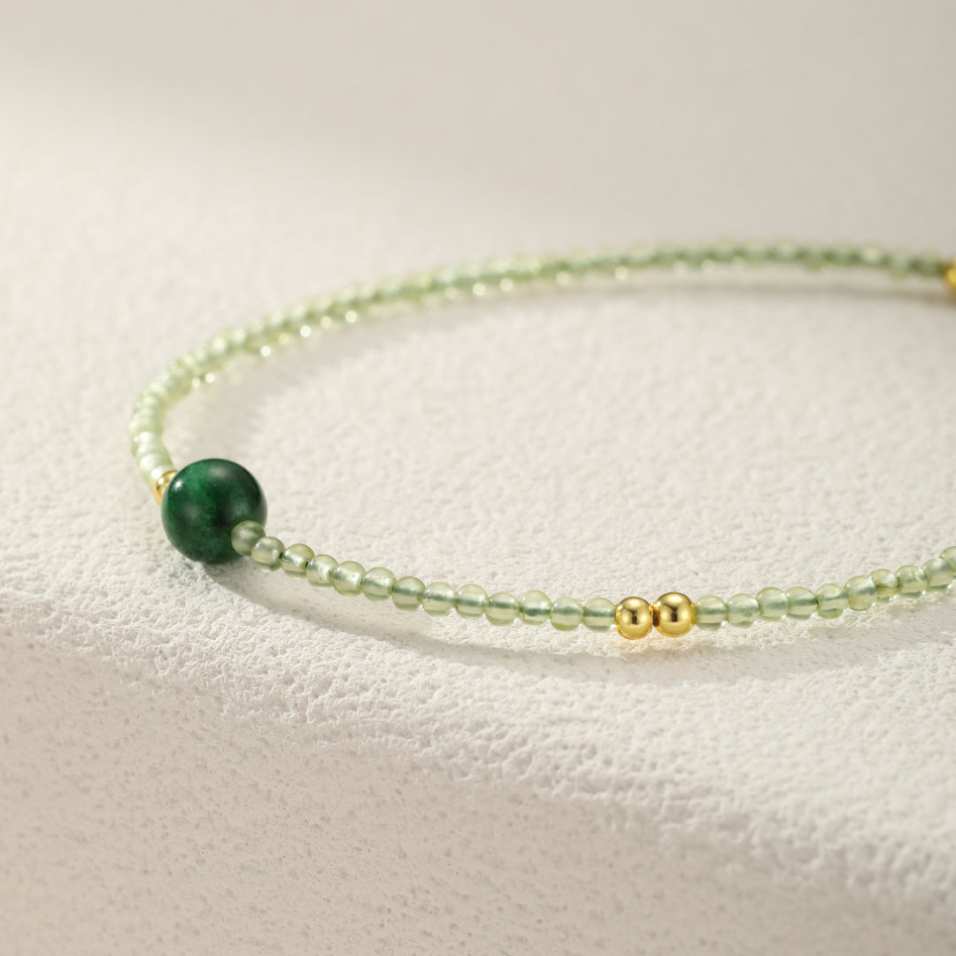 Close-up of a delicate bracelet featuring small green jade beads and gold accents, with a larger, polished green jade bead as a focal point.