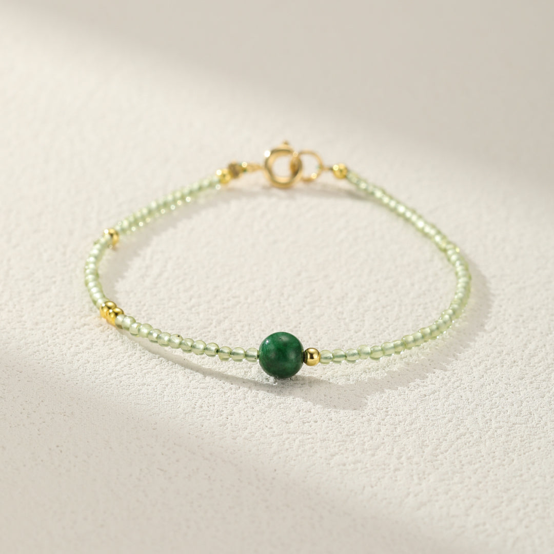 Close-up of a delicate bracelet featuring small green beads and gold accents, with a single larger green jade bead as a focal point.