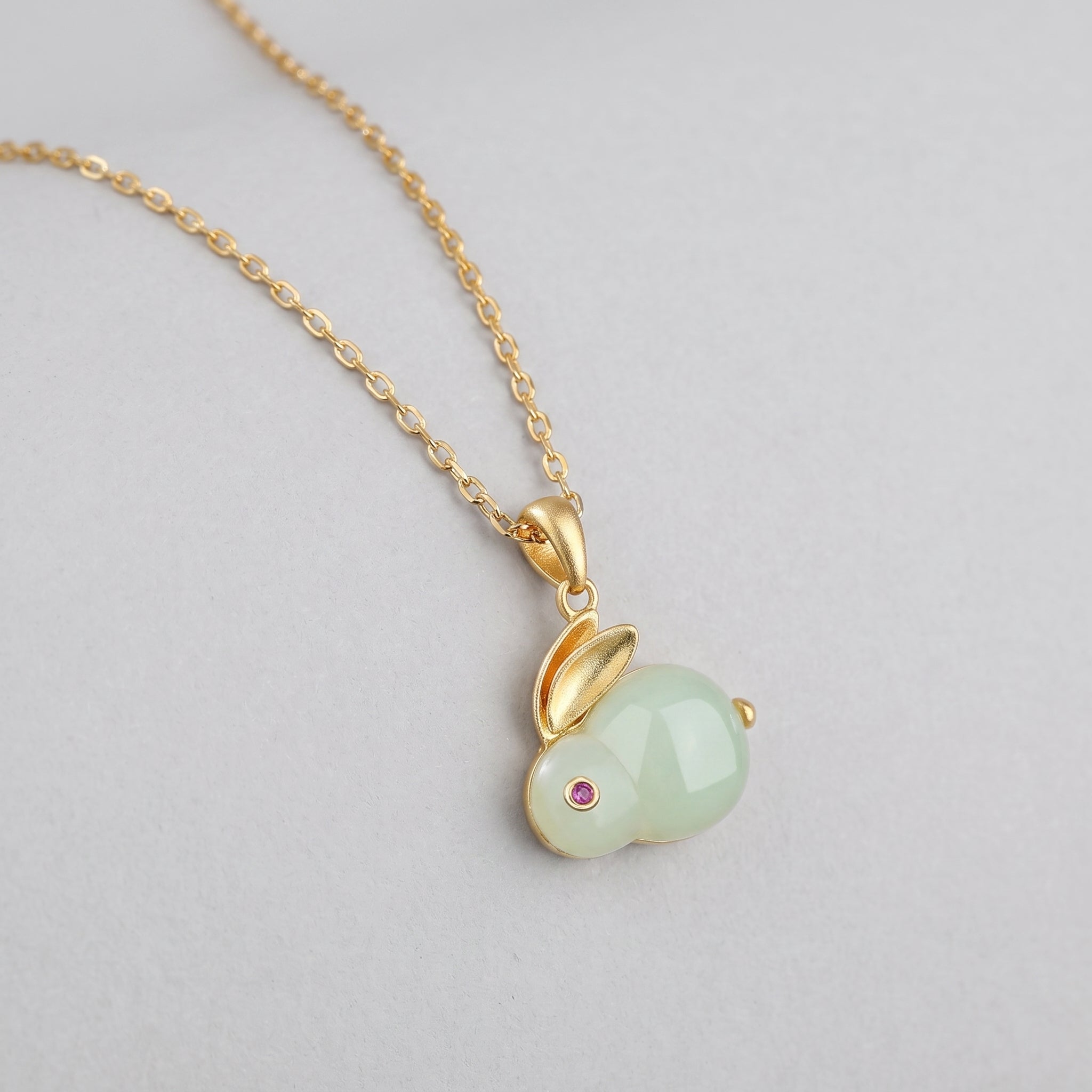 Moonglow Hetian Jade Rabbit Pendant Necklace with a small pink gemstone eye and gold chain.