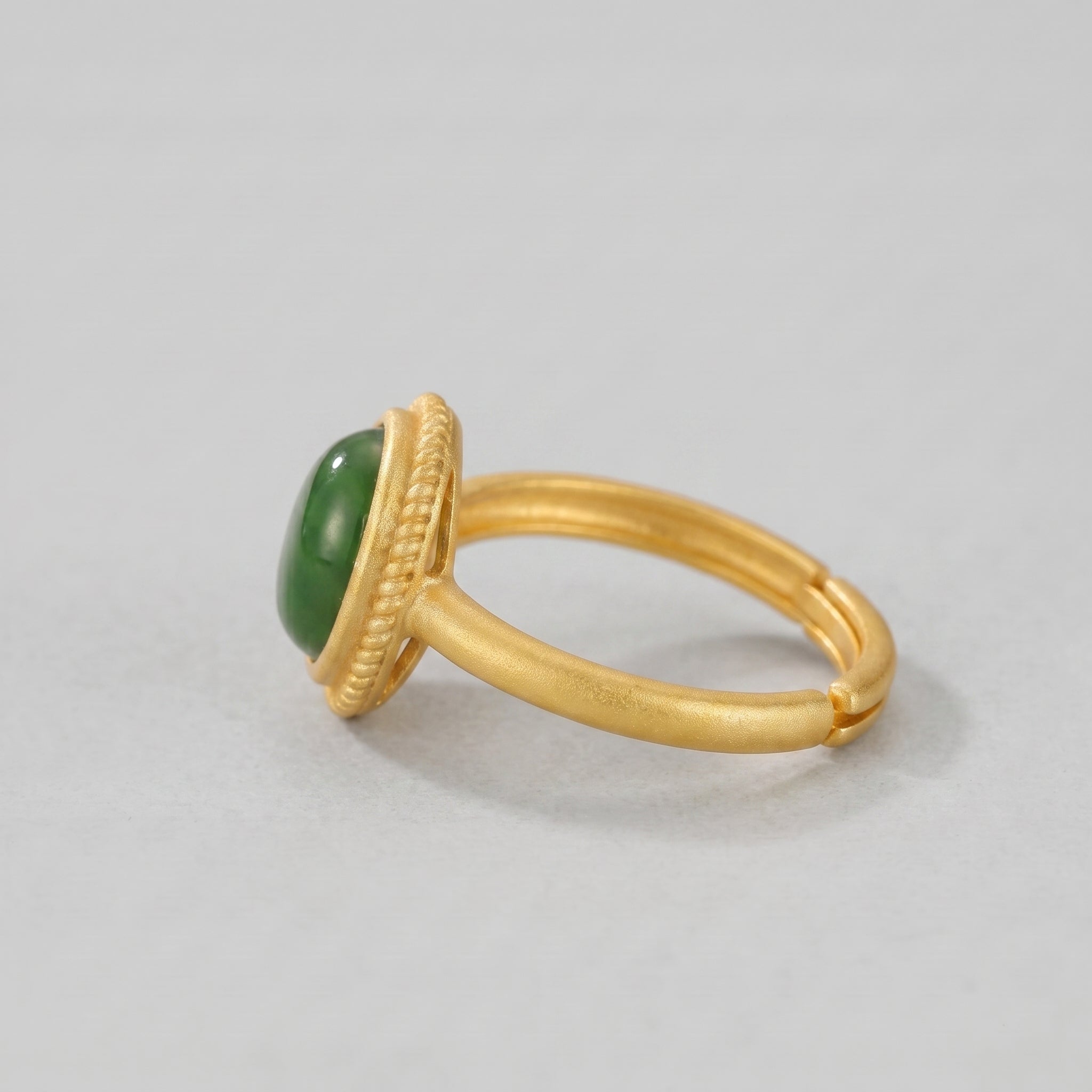 Side profile view of a New Day ring featuring a smooth, oval green jade cabochon set in a textured gold bezel and band.