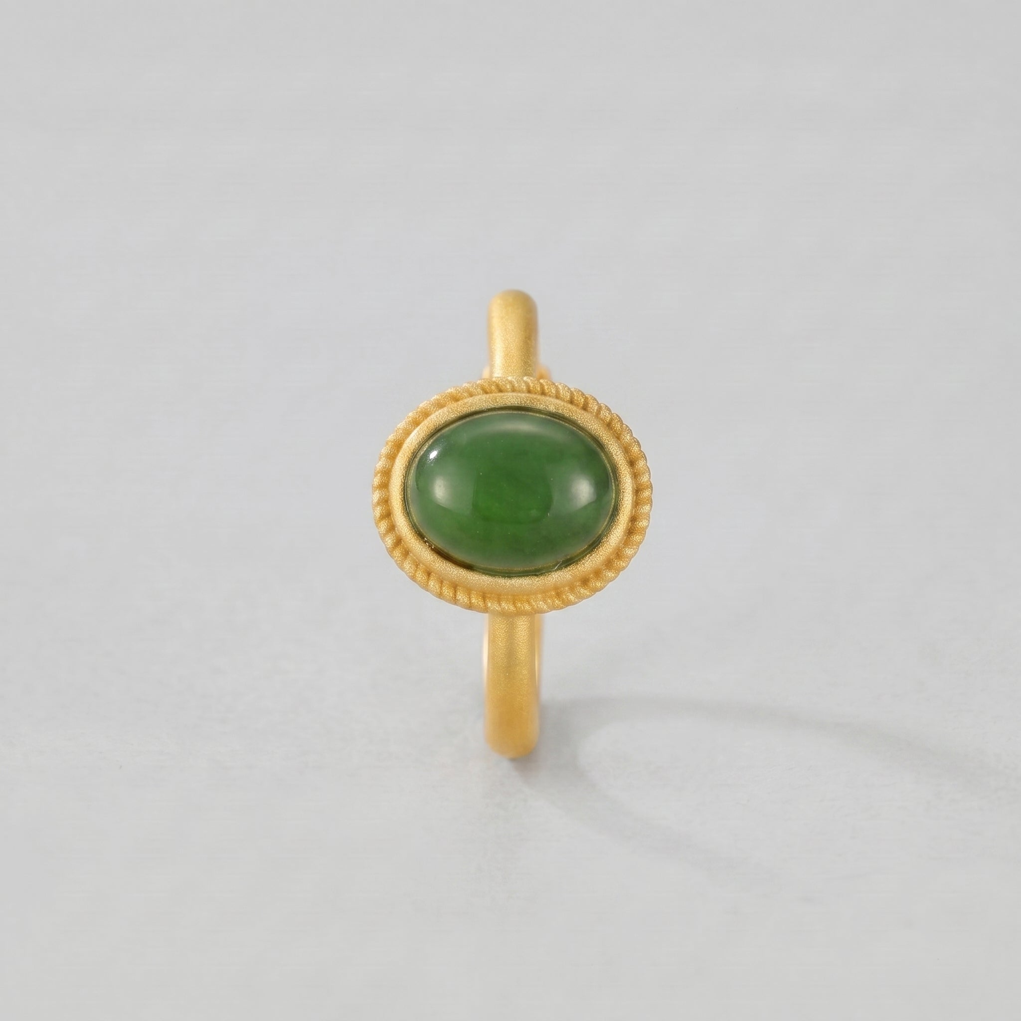 New Day gold ring featuring an oval green jade cabochon gemstone set in a twisted bezel setting on a plain gold band.