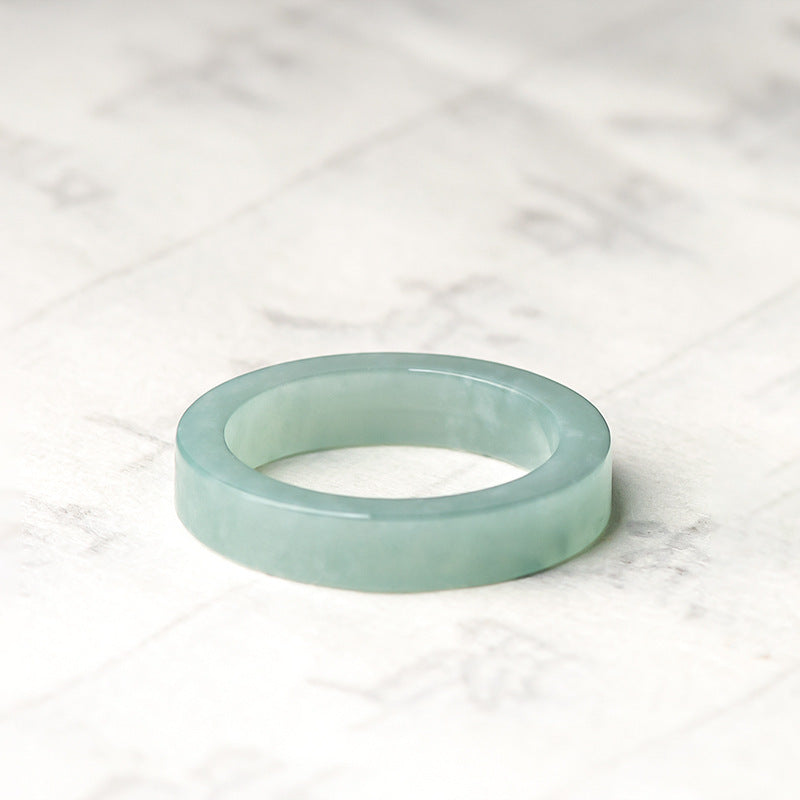 Same Sky — Ice Jade Couple Band Ring, a smooth, light green jade band ring with a flat profile, resting on a white marble surface.