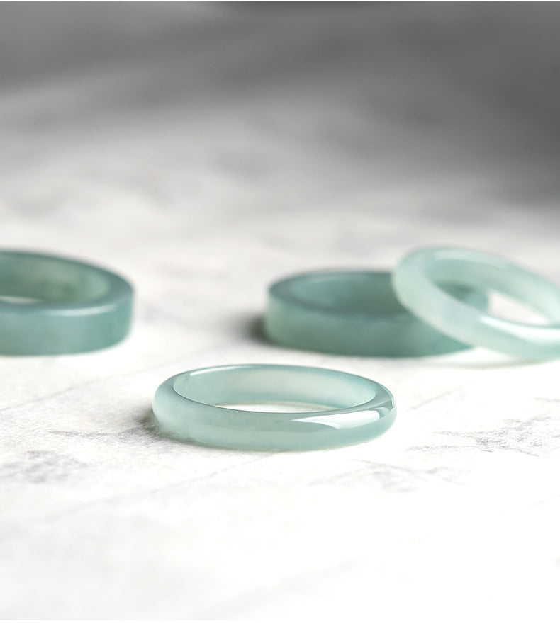 A close-up shot of several Same Sky Ice Jade couple band rings, showcasing their smooth, translucent quality and light green hue.