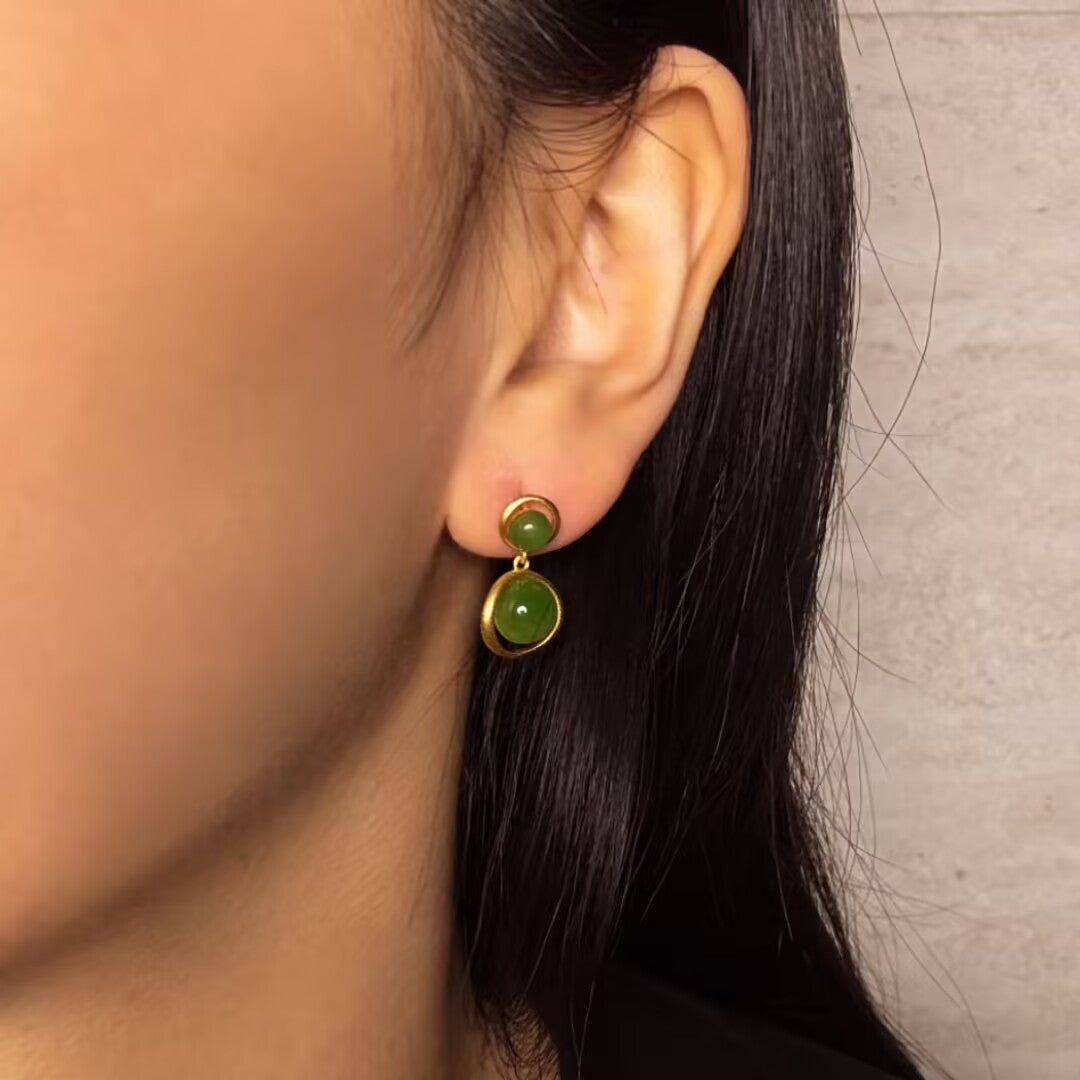 Solstice Hetian Jade Sun Drop Earrings featuring two green jade cabochons set in gold-plated silver, dangling from the ear.