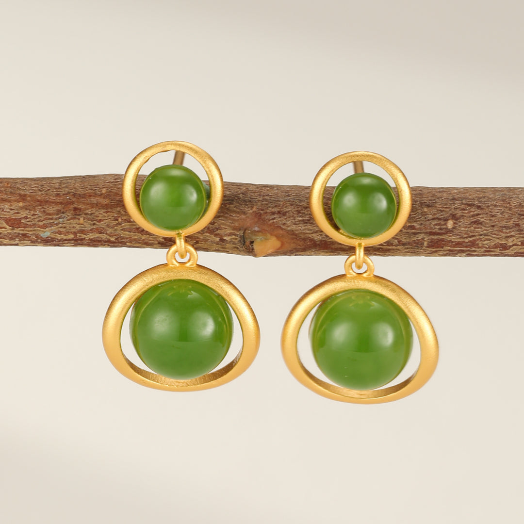Solstice Hetian Jade Sun Drop Earrings featuring two green jade beads, one smaller at the top and one larger at the bottom, suspended in gold-plated silver frames against a neutral background.