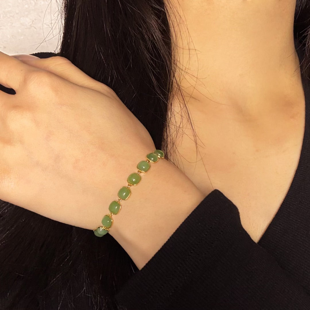 A woman wears the Sunday Best Green Jade Link Bracelet on her wrist. The bracelet features square-cut green jade stones linked together with gold-plated metal.