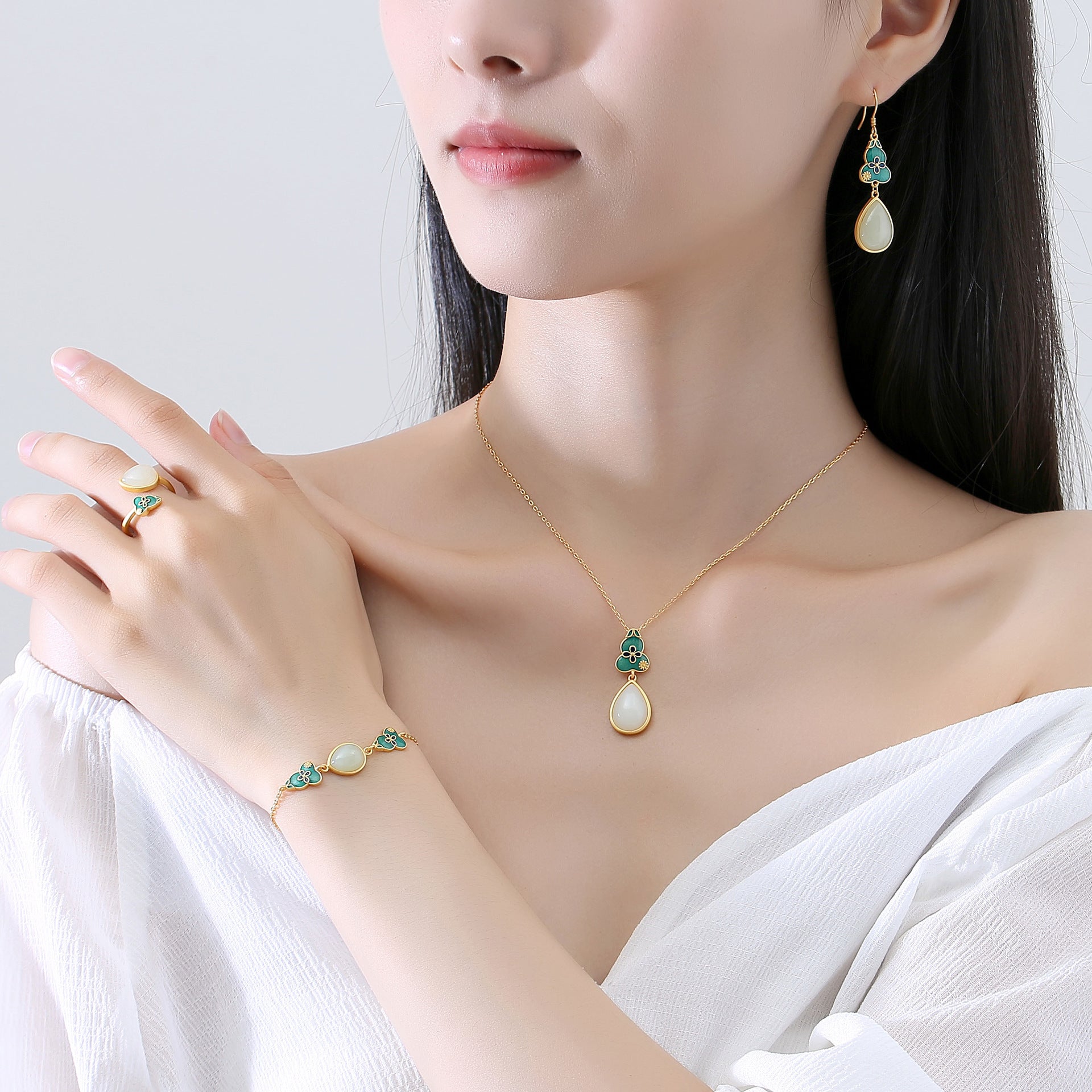 A woman models a delicate gold jewelry set featuring carved jade gourds and pear-shaped jade pendants, including earrings, a necklace, a bracelet, and a ring.